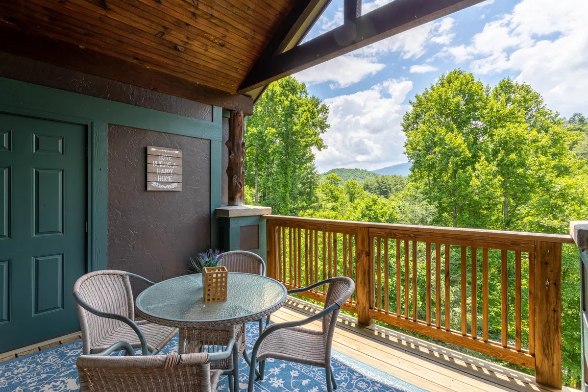 A serene outdoor seating area featuring a round glass table with woven chairs and a decorative plant, all set against the backdrop of expansive mountain views. The scene invites guests to relax, enjoy morning coffee, or unwind with loved ones while taking in the fresh mountain air and natural beauty.