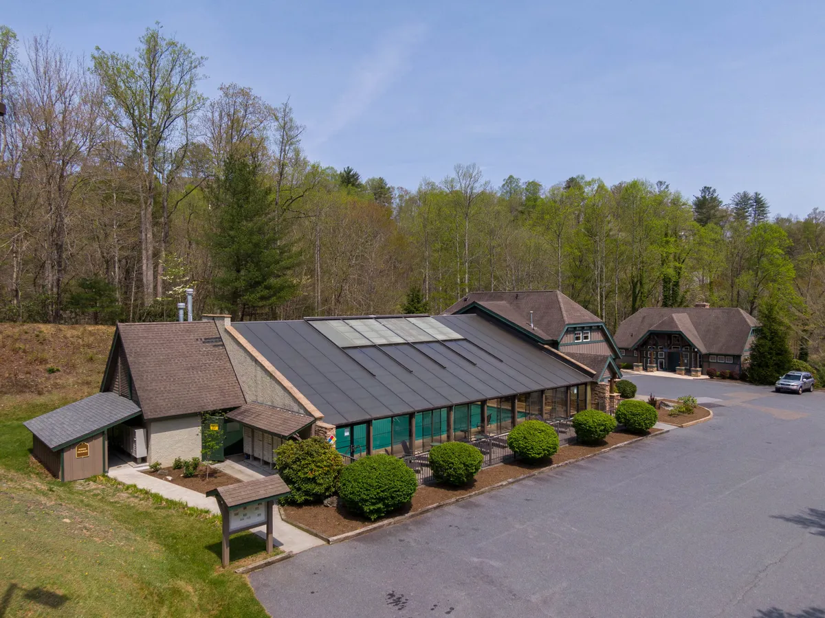 This image features the main building of the community, characterized by its large windows, solar panels on the roof, and the lush greenery that surrounds it. The scene suggests a space designed for gatherings, outdoor events, and enjoying nature together.