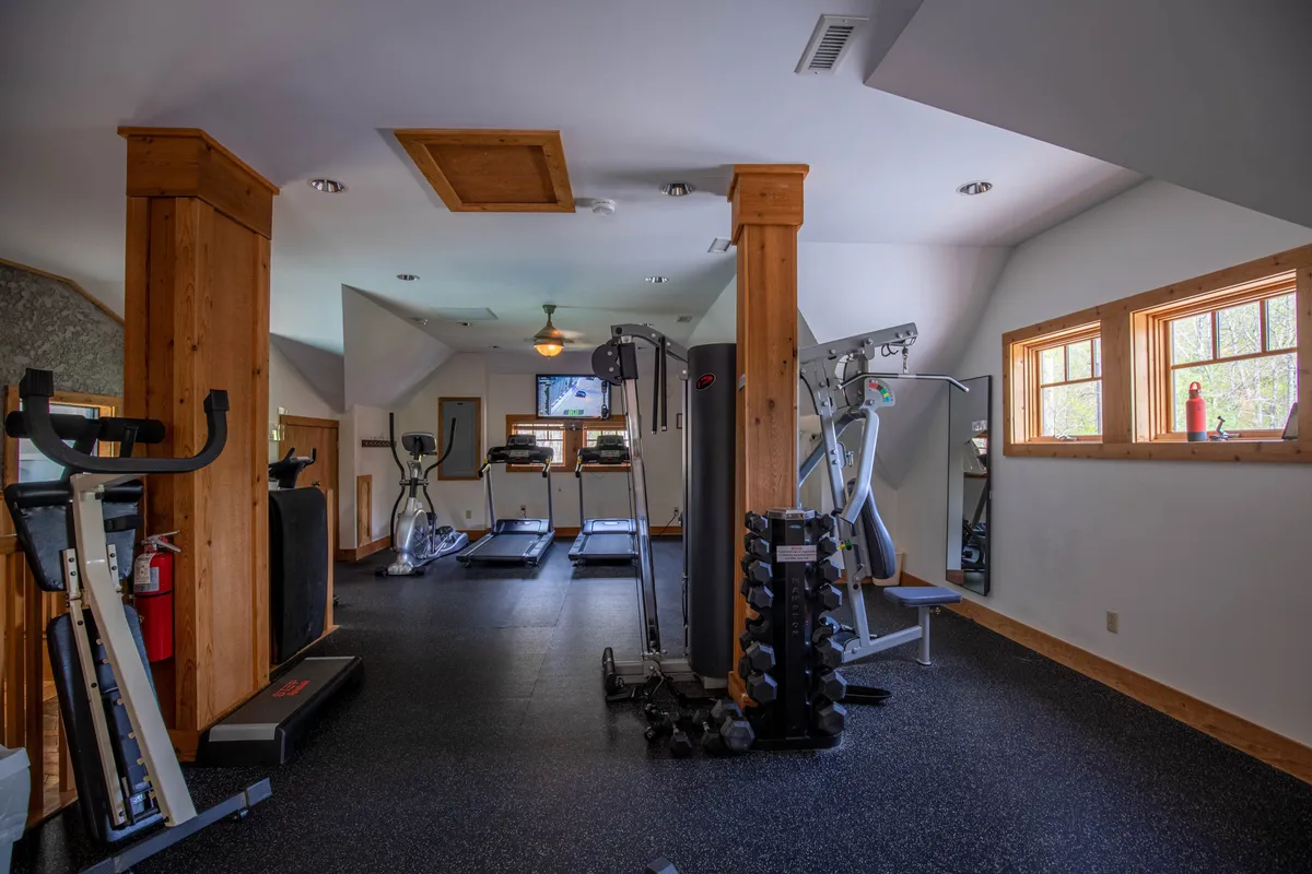 A modern fitness room filled with treadmills, a weight rack, and exercise machines. Natural light pours in through the windows, and the arrangement is suitable for both solo and group activities.