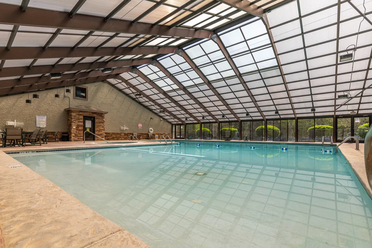 An inviting indoor swimming pool bathed in natural light from a glass ceiling, surrounded by lounge chairs. The tranquil setting offers a refreshing escape, ideal for soothing tired muscles after a day spent outdoors.