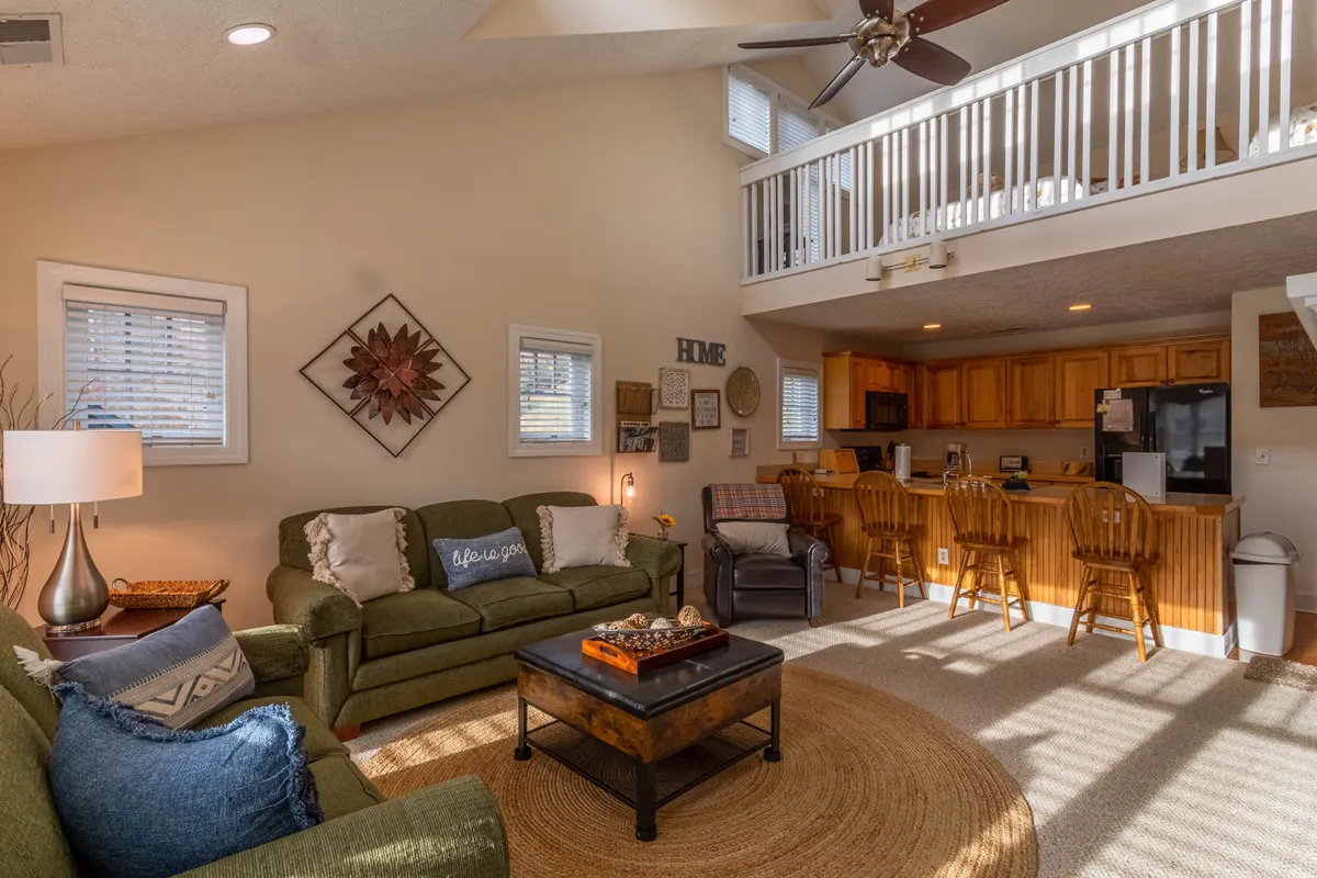 A bright, inviting living space featuring a comfortable green sofa, a decorative coffee table, and an open kitchen in the background. Natural light pours in, enhancing the cozy and welcoming vibe perfectly suited for family or friends to gather.