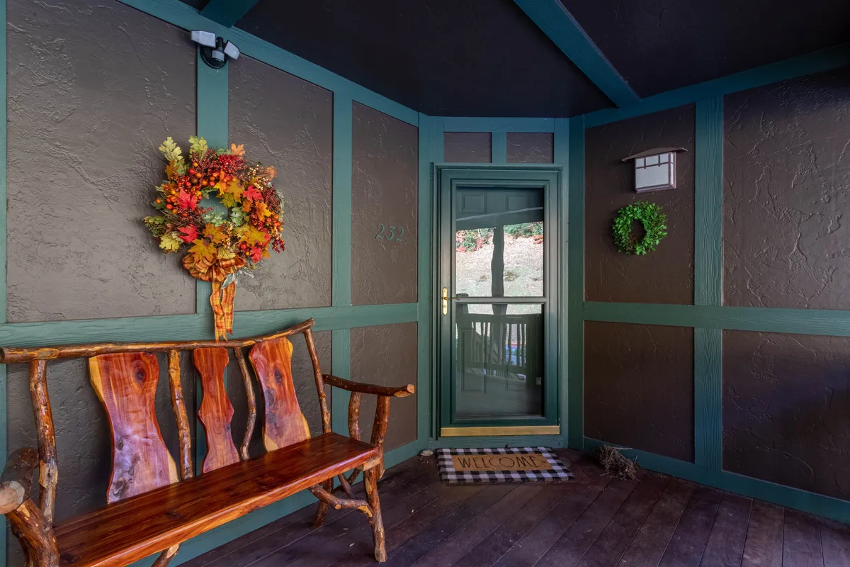 A rustic wooden bench and a colorful wreath create a warm, inviting entrance to the home. The welcome mat and natural textures suggest guests arriving and gathering at the threshold.