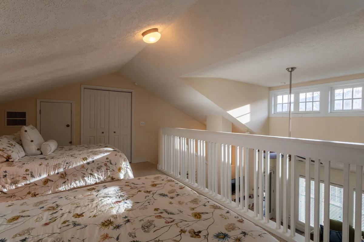 A loft space with both queen and full beds, floral bedding, and a railing that overlooks the lower living area. Large windows let in natural light and offer views, while the open yet secluded layout offers both privacy and connection to the rest of the home.