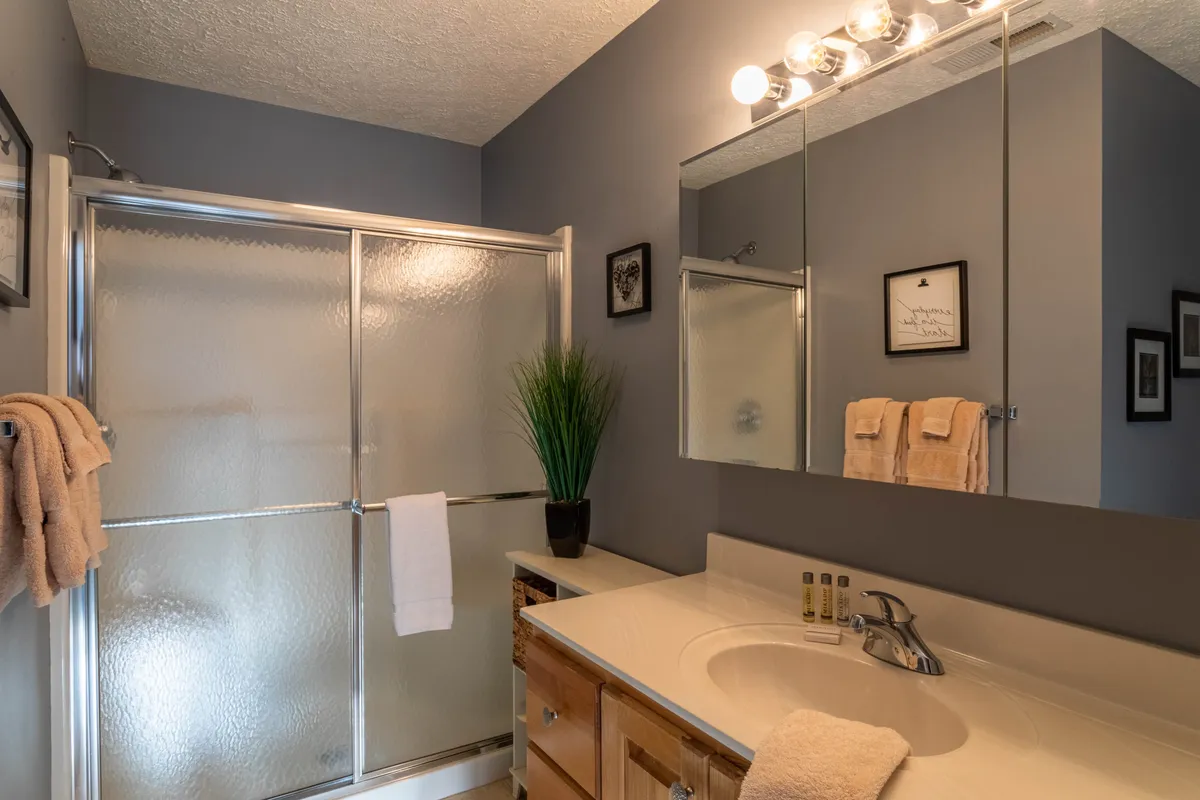 A bright, modern bathroom with a spacious vanity, large mirror, and a glass-enclosed shower. The design is fresh and uncluttered, with morning light illuminating the space and creating a serene feel.