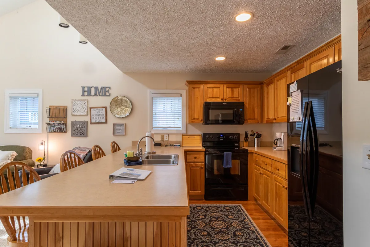 Another angle of the kitchen showcases a kitchen island, wood cabinetry, black appliances, and decorative wall art. The mood is cozy and inviting, illustrating how the kitchen serves as a central gathering point for cooking and entertaining guests.